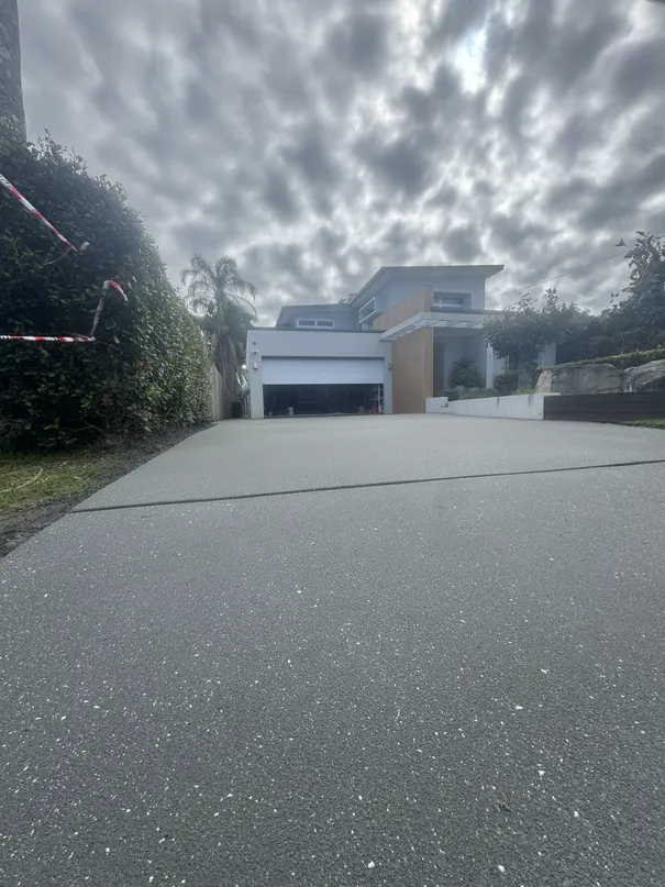 Driveway resurfaced with Prime Resin spray resin in Ironstone with Arctic White and Night Sky fleck, leading to a modern two-storey home